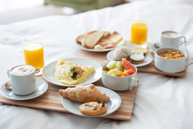 Close up of coffee, omlet, fruit, pastries and cereal on the hotel bed.