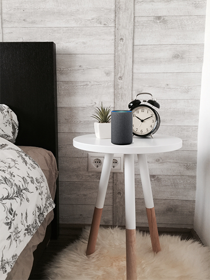 Dark grey third generation echo resting on the nightstand with a vintage alarm clock and succulent plant.